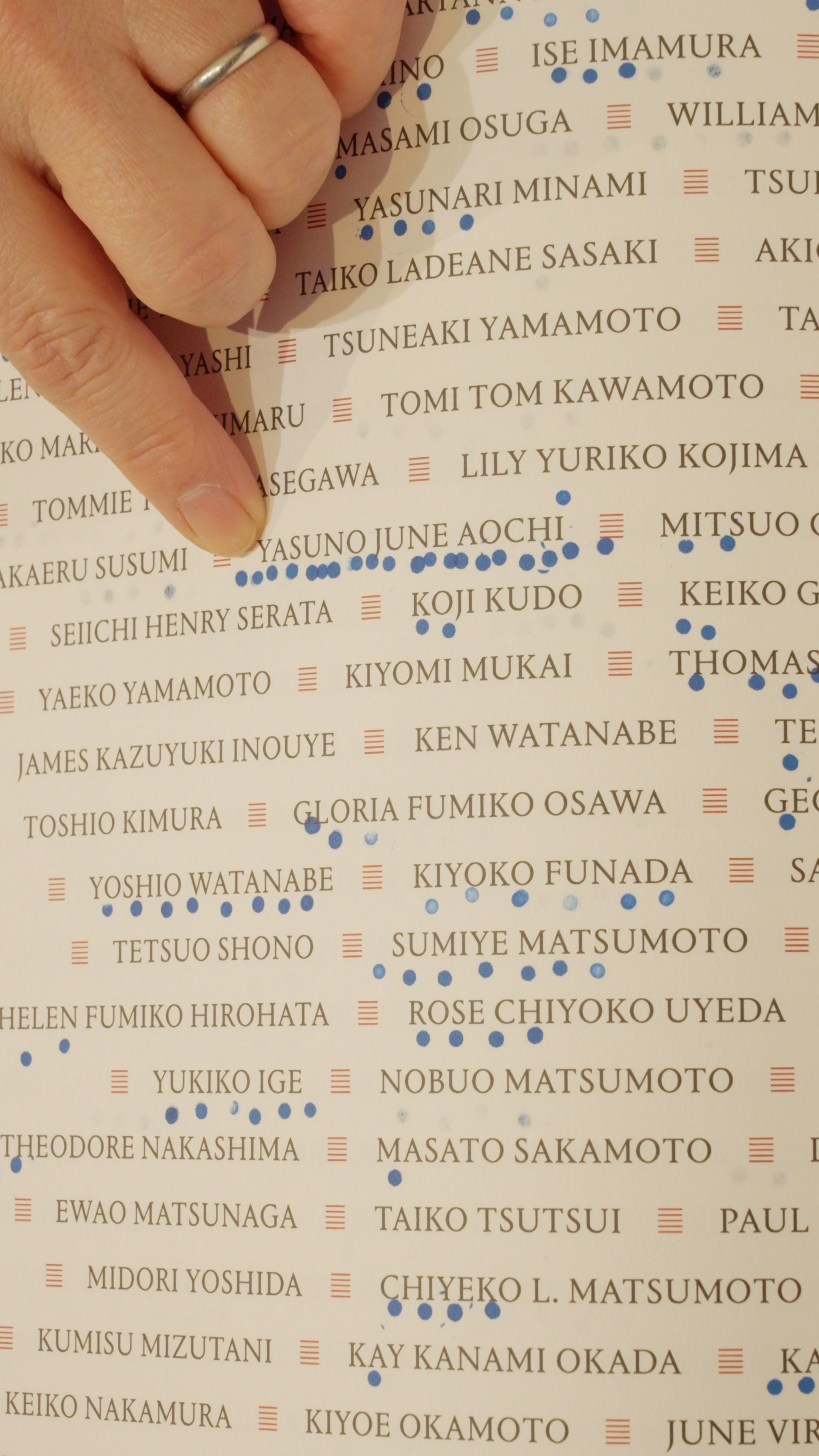 A finger points to one among a list of names with several blue dots next to it.