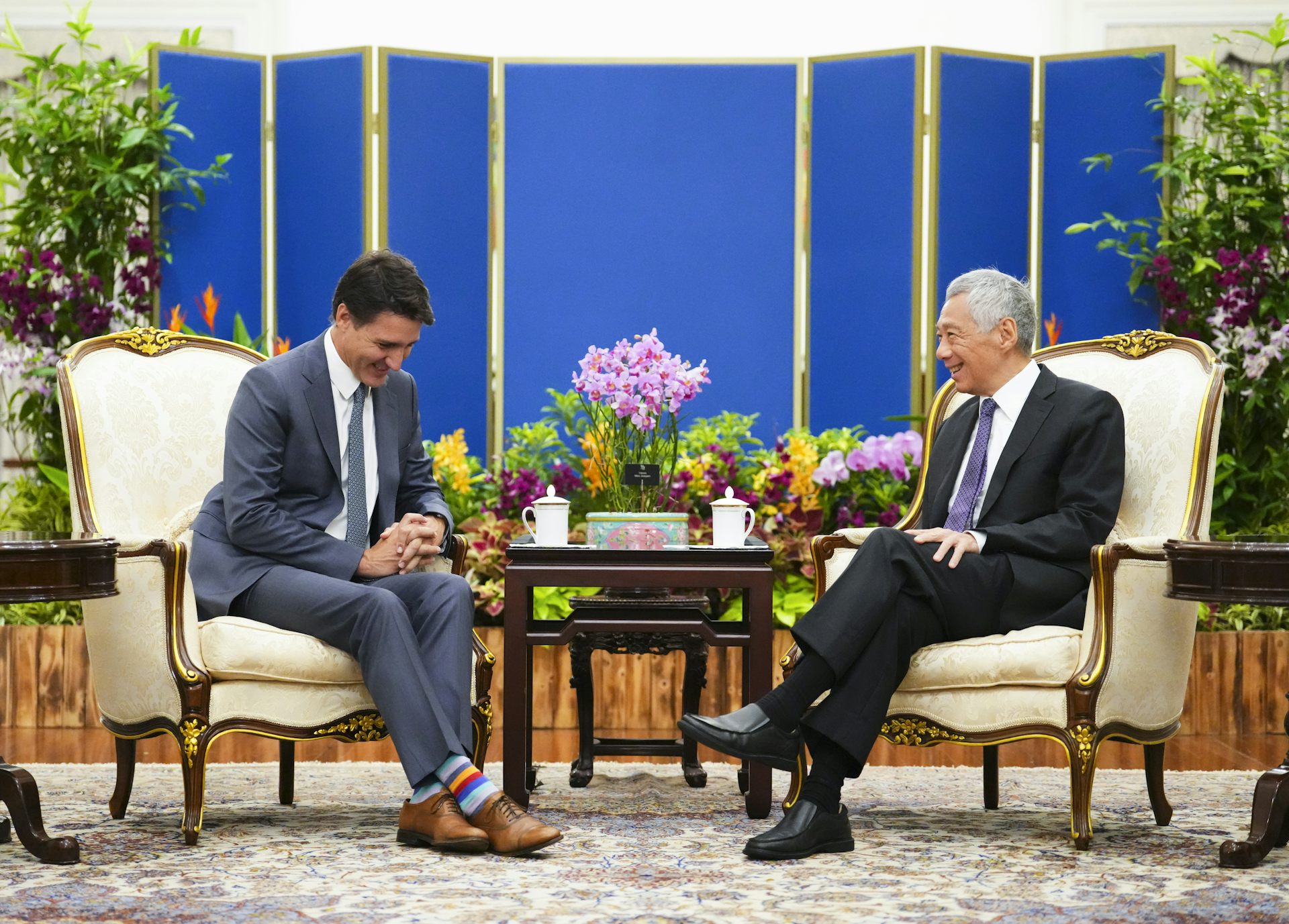 Two men, one white and one Asian, sit on a set of cream-coloured armchairs while having a conversation