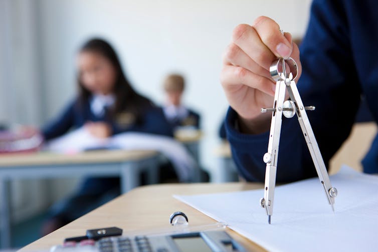 A student holds a compass on a desk. A calculator rests near by.