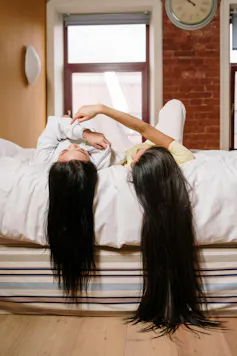 Two people lay on the end of a bed. One has much longer hair.