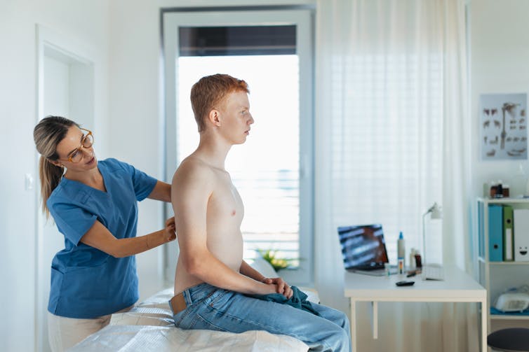 clinician checks the back of a young man with red hair and freckles in health office