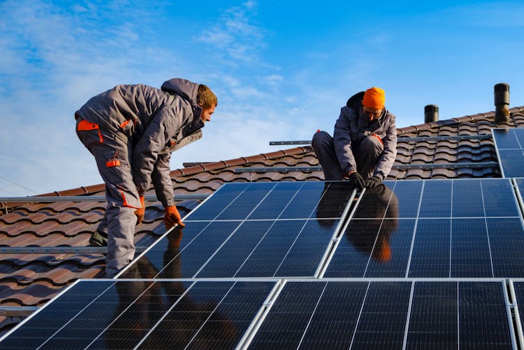 two men install solar panels on roof