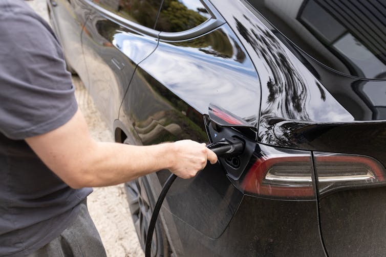man puts charger in electric vehicle