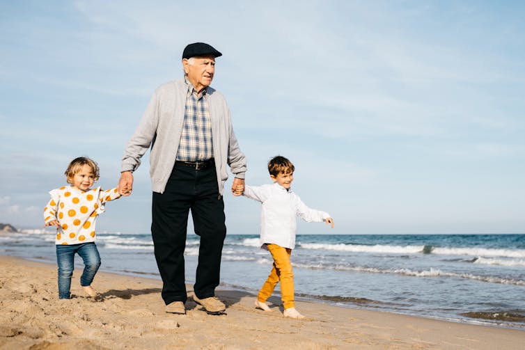 Grandfather strolling with his grandchildren hand in hand on the beach.