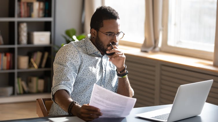 Man concentrates on computer, holding sheet of paper