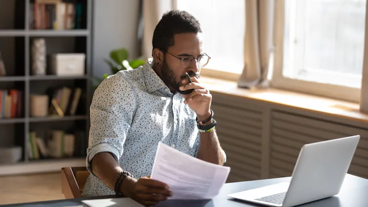 Man concentrates on computer, holding sheet of paper