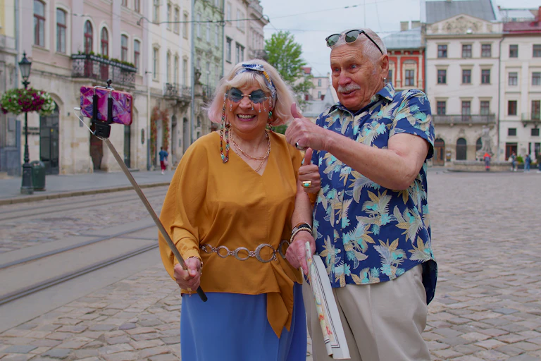 Elderly man and woman walking in a city centre with smartphone on selfie stick.