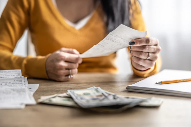 Woman sitting at a table with banknotes, till slips, paper pad and pencil