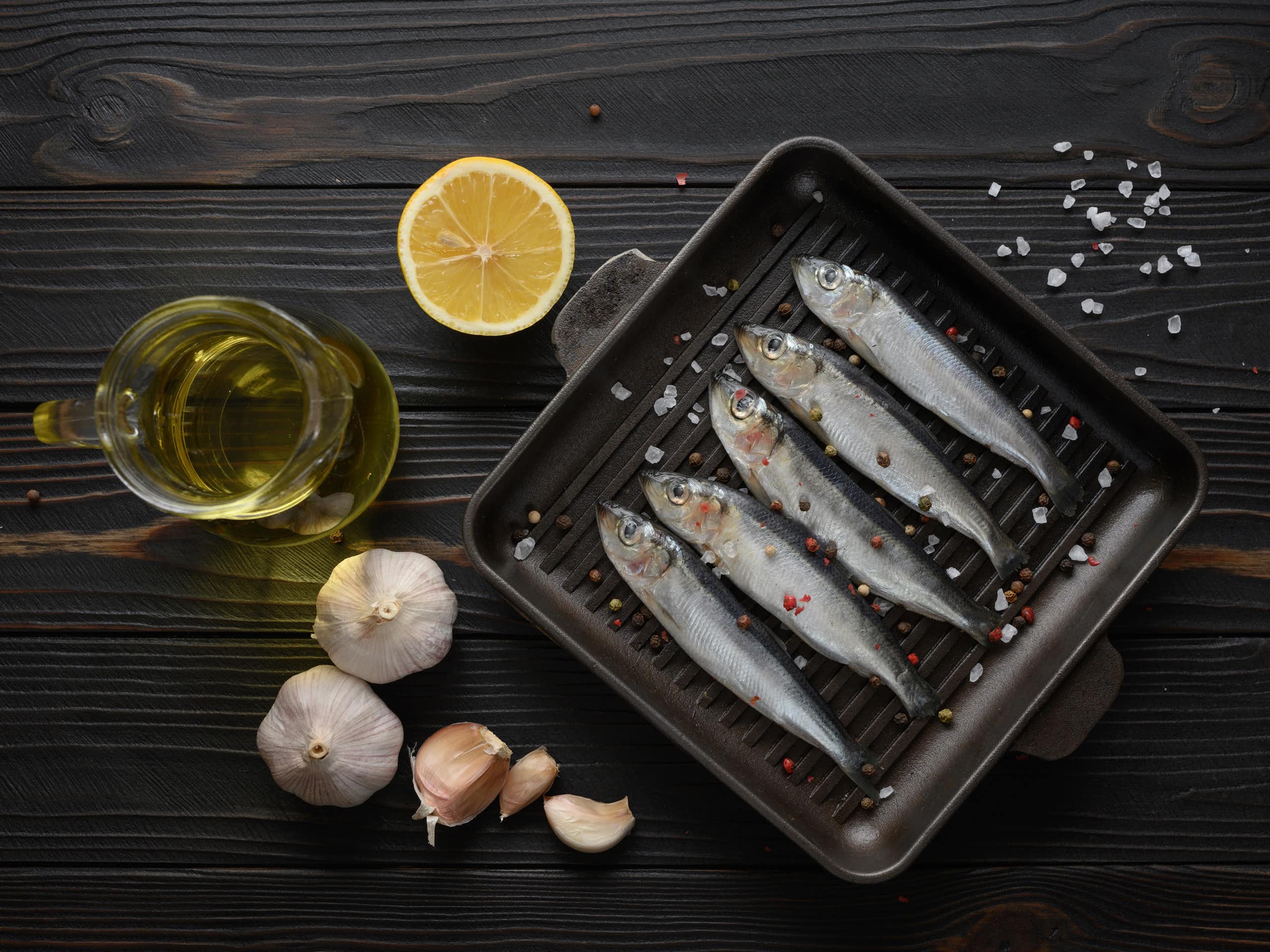A combination of raw sardines, garlic, lemon and a bottle of oil.