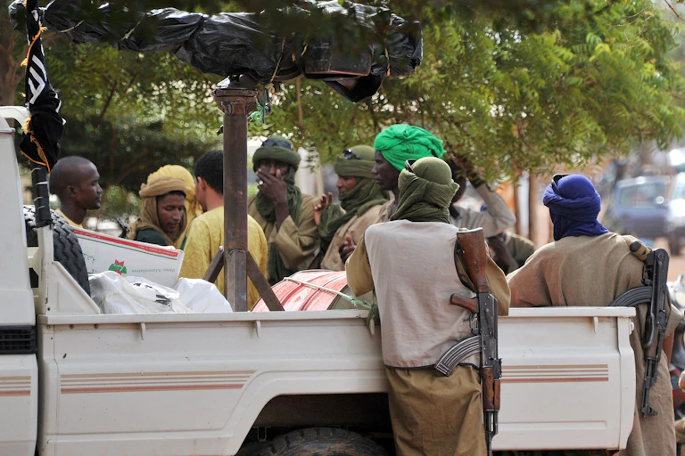 Men holding rifles, gathered around a pick up truck.