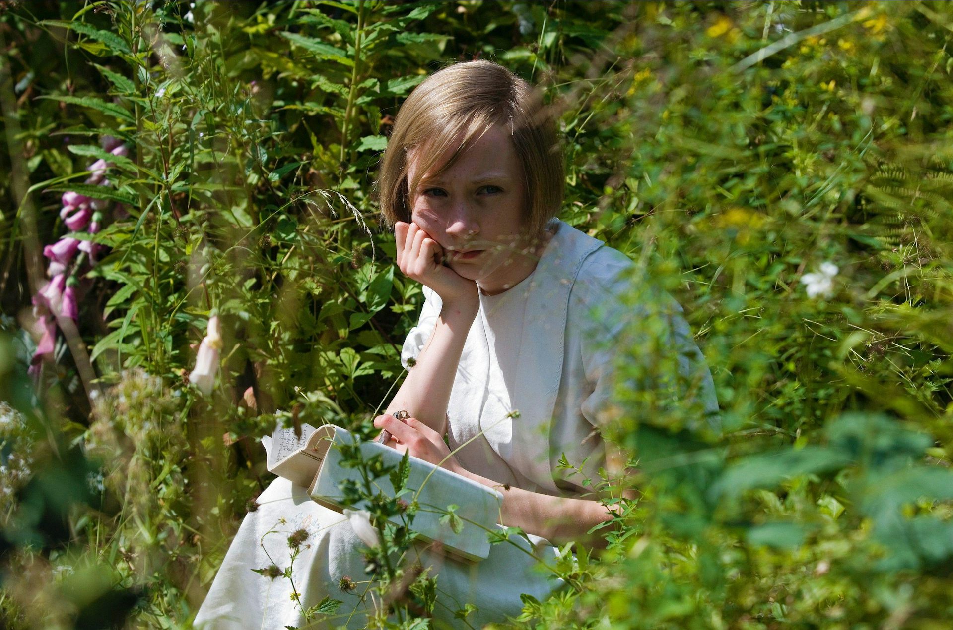A young girl sat reading in a garden.