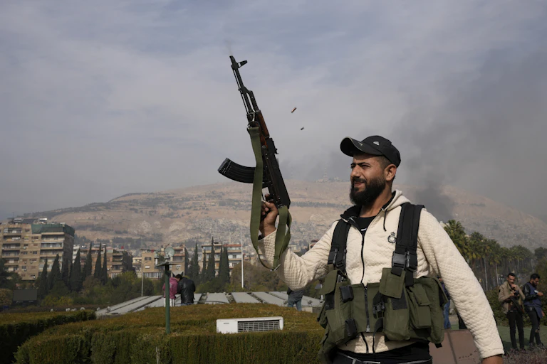A bearded fighter smiles as he fires his AK-47 over his head.