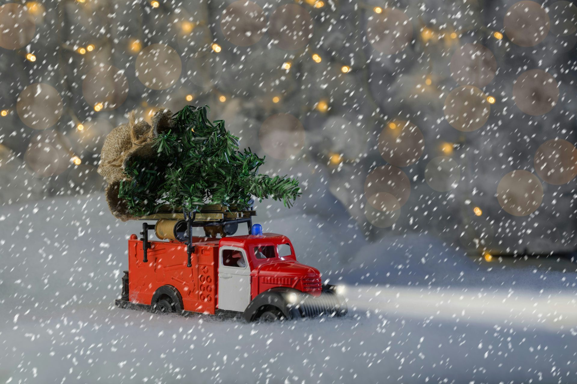 Un camion rouge transporte un sapin de Noël sous une tempête de neige.