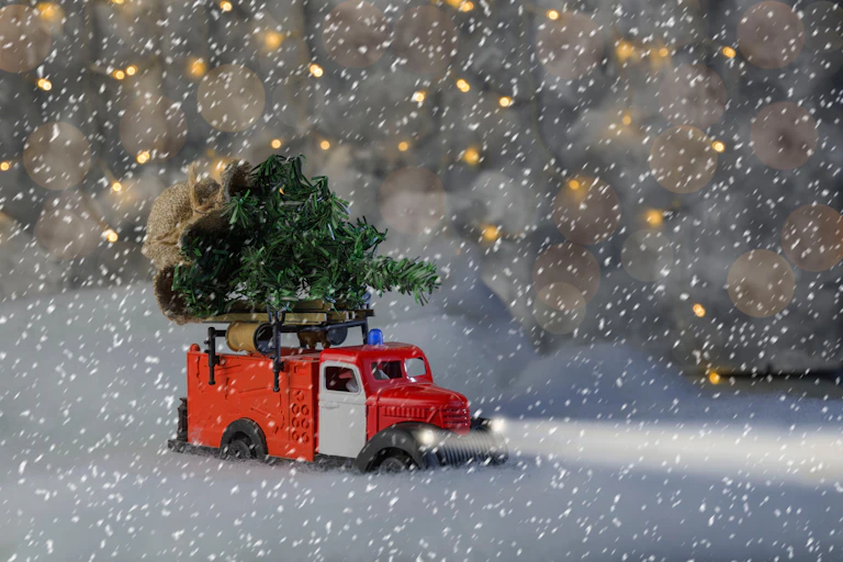 Un camion rouge transporte un sapin de Noël sous une tempête de neige.