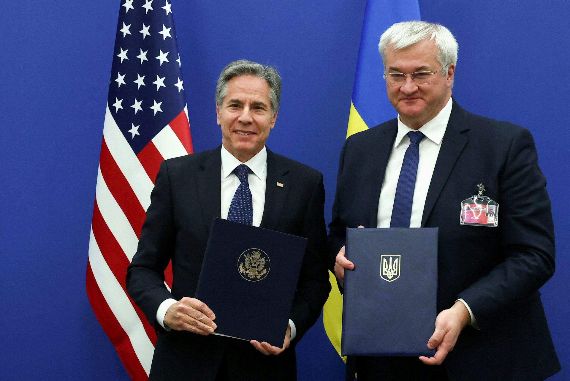 US secretary of state, Antony Blinken, and Ukraine's foreign minister, Andrii Sybiha holding folders and standing in front of their national flags.