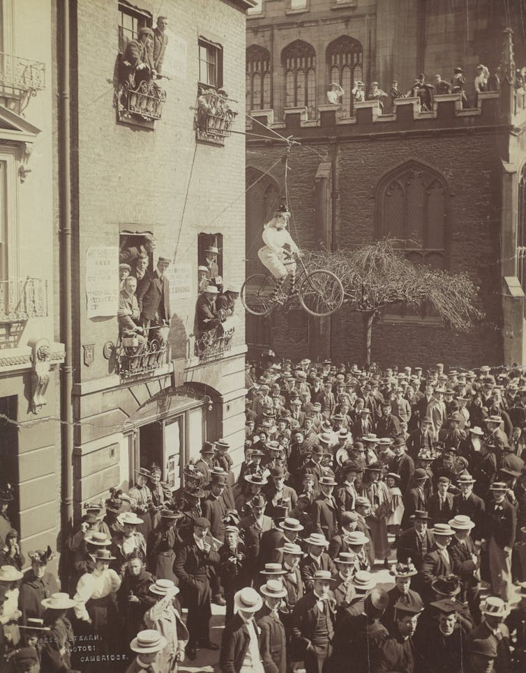 A crowd with an effigy of a woman riding a bike above them.