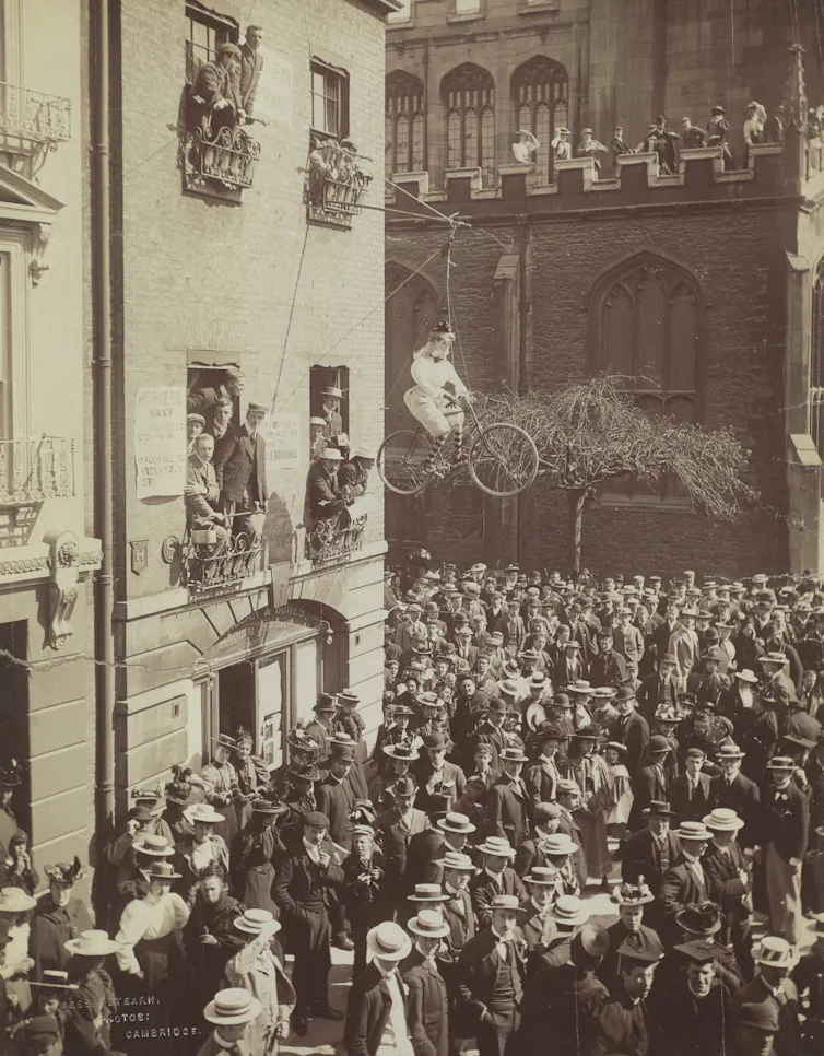 A crowd with an effigy of a woman riding a bike above them.
