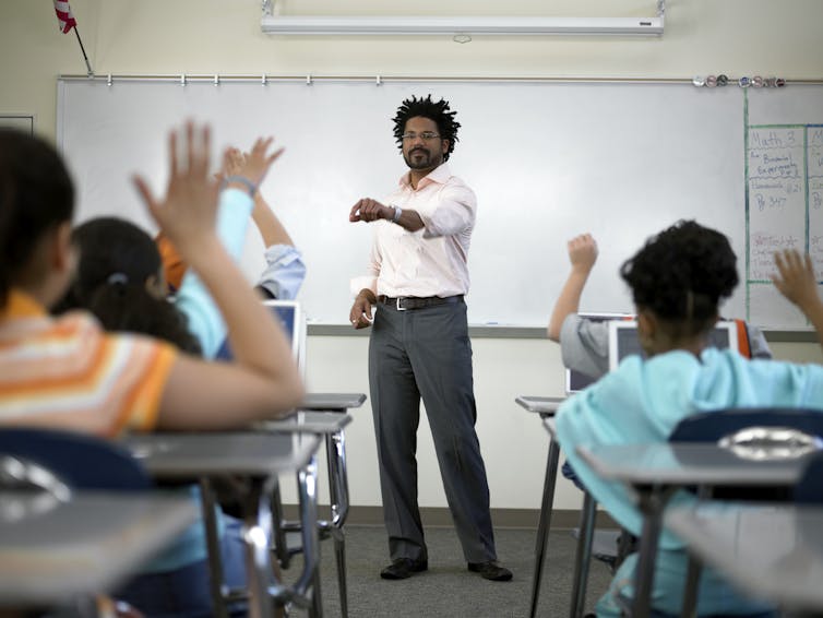 Black male teacher stands in front of classroom and points to student with hand raised