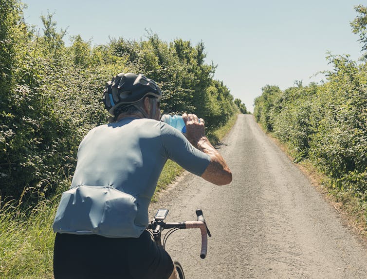 A man riding a bike while drinking a blue sports drink.
