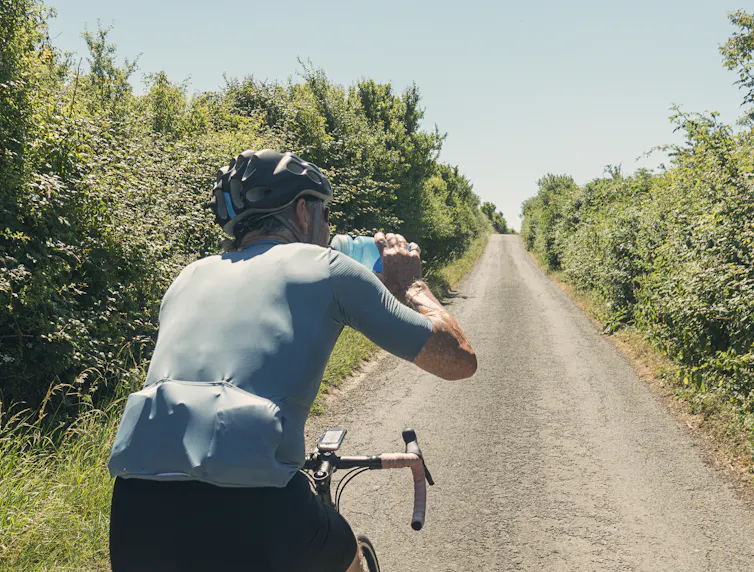 A man riding a bike while drinking a blue sports drink.