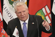 A rotund man with thinning white hair in a blue suit and tie.