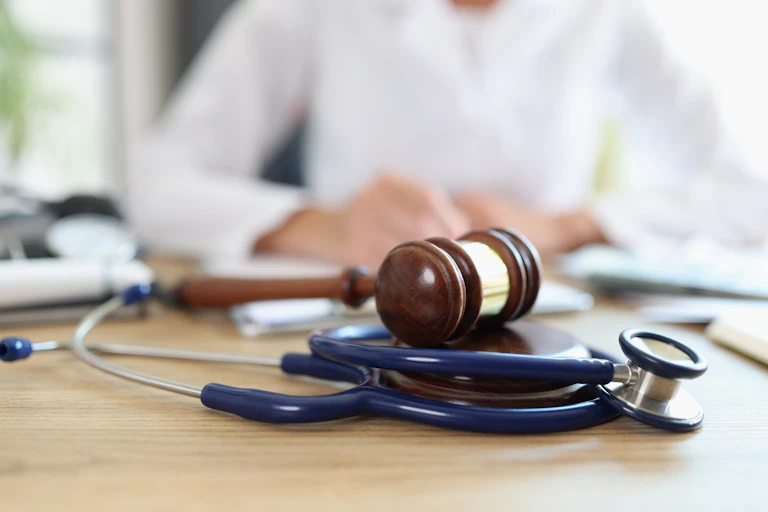 A gavel and stethoscope, with a person in a white coat out of focus in the background
