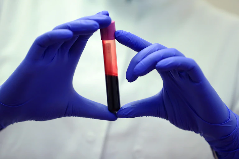 Nitrile gloved hands holding a half full tube of blood