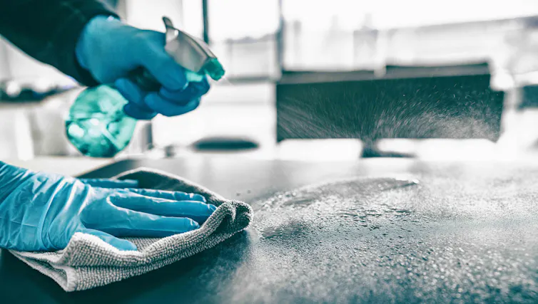 Gloved hands spraying and wiping a surface.