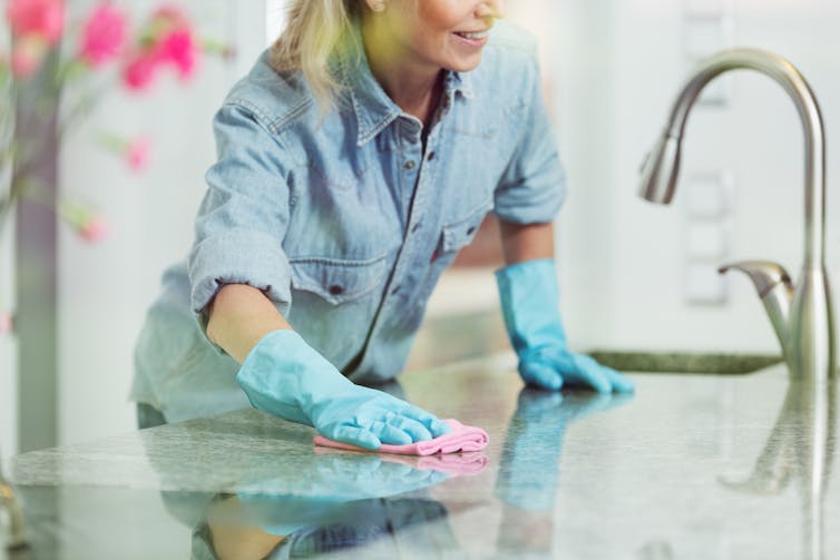 A woman wipes the kitchen counter with a pink cloth.