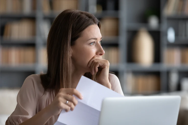 A woman holds a piece of a paper and looks over her shoulder in concern.