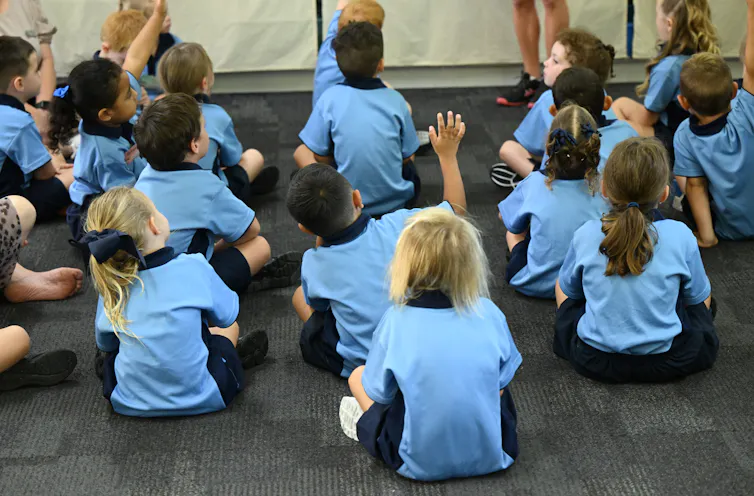 A group of young children in uniform sit on the floor.