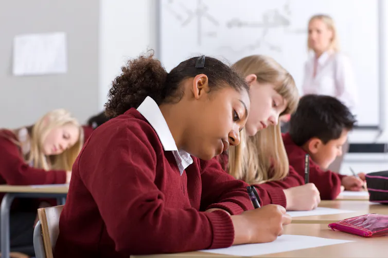 A sideview of students in uniform writing at desks.