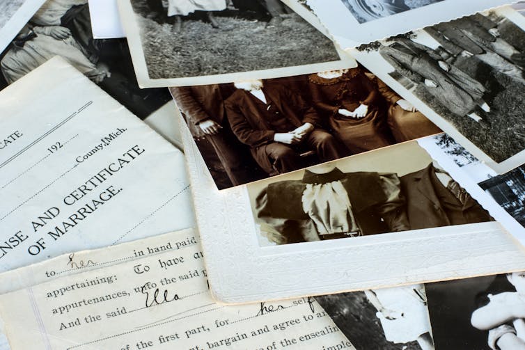A pile of black-and-white photographs and yellowed documents seen on a table