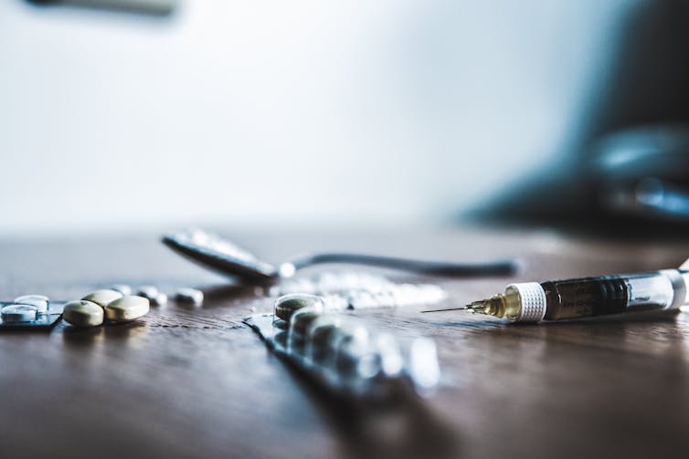 Pills, tablets, a teaspoon and a syringe on a table for drug use