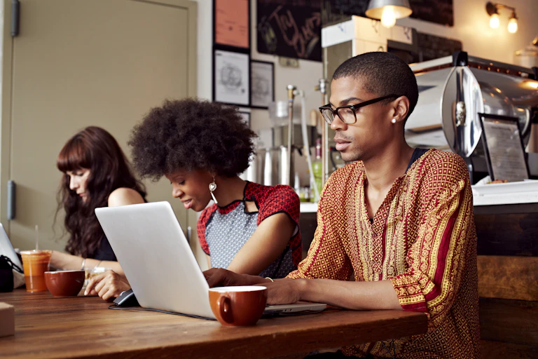 Three young people seated at a table with cups and a laptop