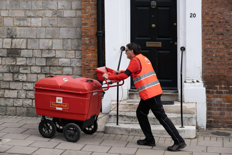 A postal worker pushing a trolley past a house with the number 20 on it.