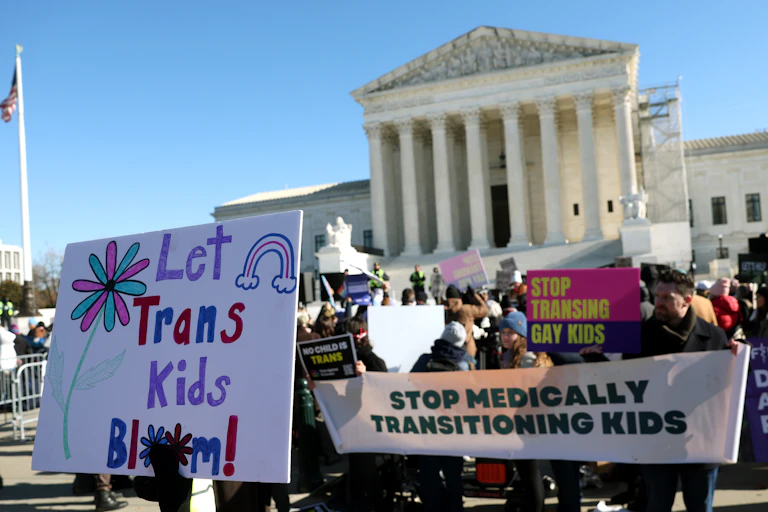 People carrying large signs either supporting or opposing trans kids.