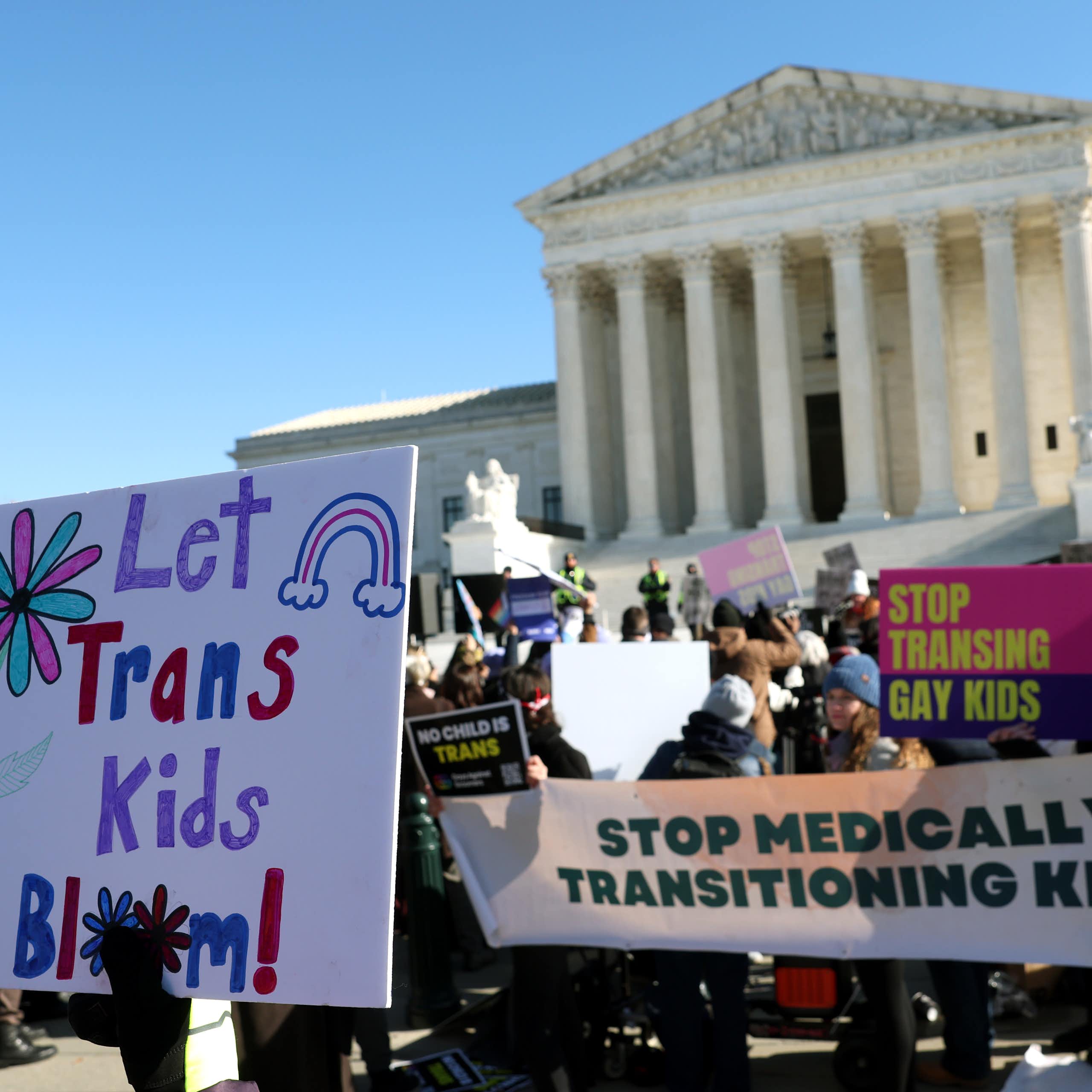People carrying large signs either supporting or opposing trans kids.
