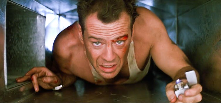 Bruce Willis crawls through an air conditioner duct wearing a dirty vest and holding a lighter.