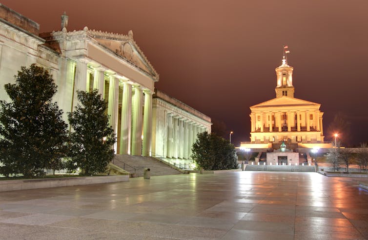 Two large white buildings with columns, on two sides of a large plaza.