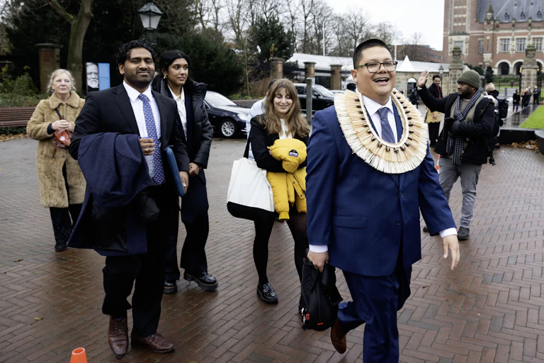 A lawyer with a traditional Vanuatu grass band around his neck leaves the ICJ with his legal team