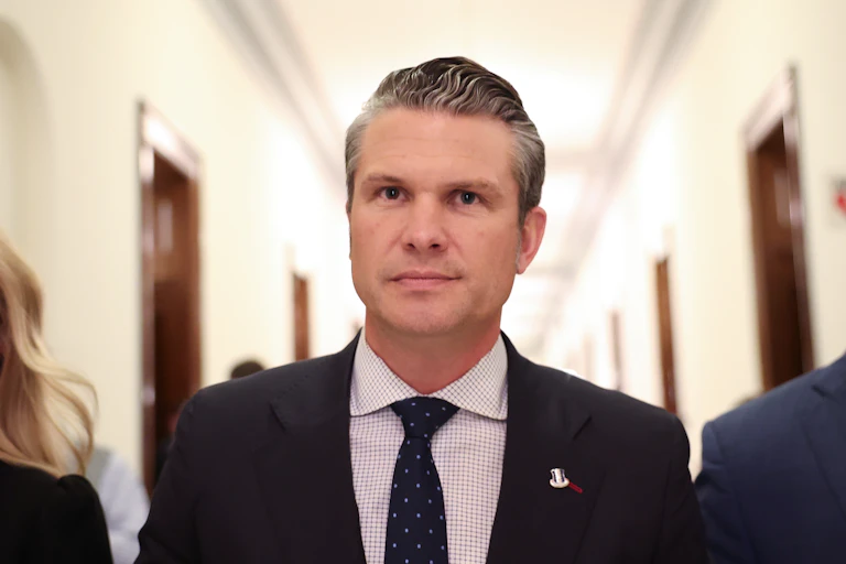 A man in a black suit and a polka dot tie, standing in a hallway.