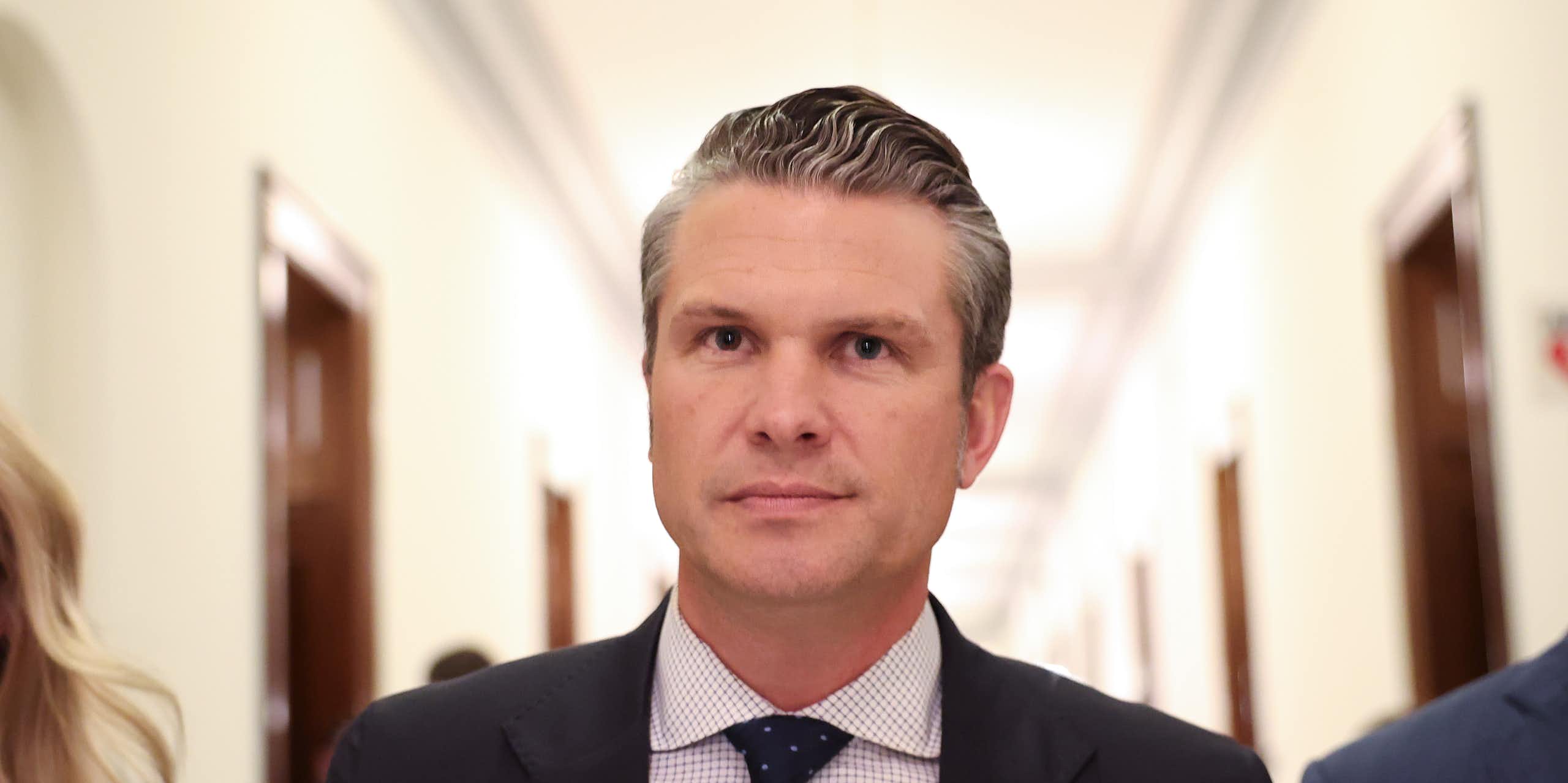 A man in a black suit and a polka dot tie, standing in a hallway.