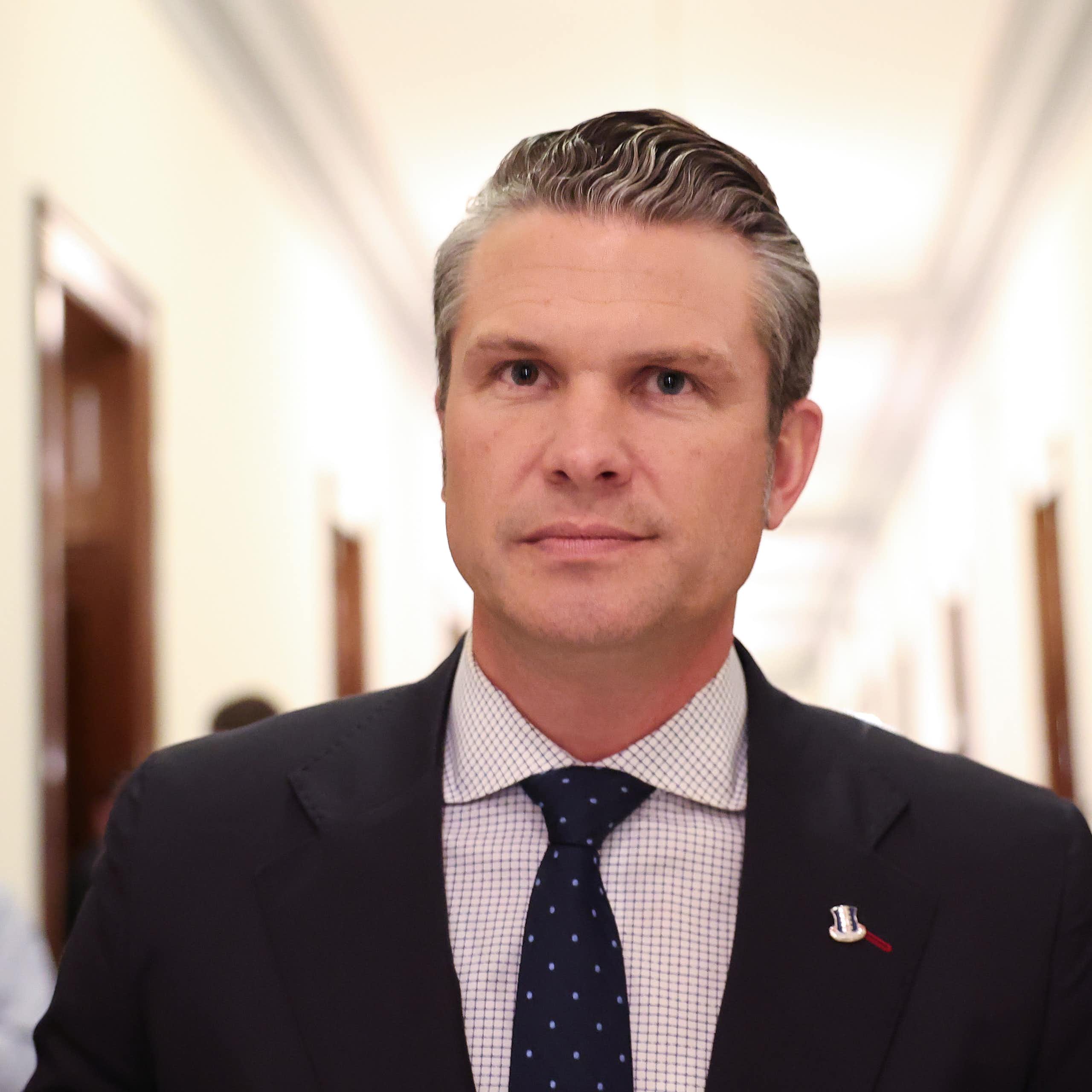 A man in a black suit and a polka dot tie, standing in a hallway.