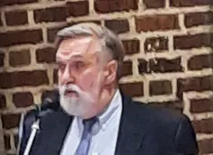 A gray-haired man in a black suit speaking at a lectern.