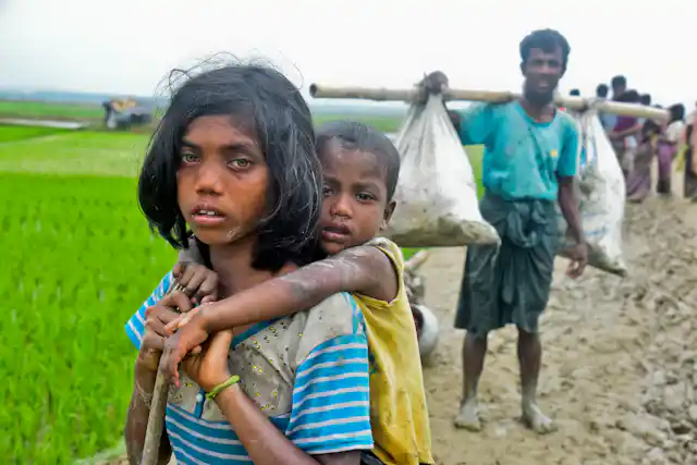A young girl with a child clinging onto her back walk down a muddy path.