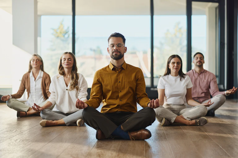 Five people doing meditation with their eyes closed while being seated in a lotus position.