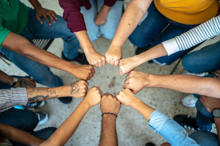 A group of people form a circle with their clenched fists.