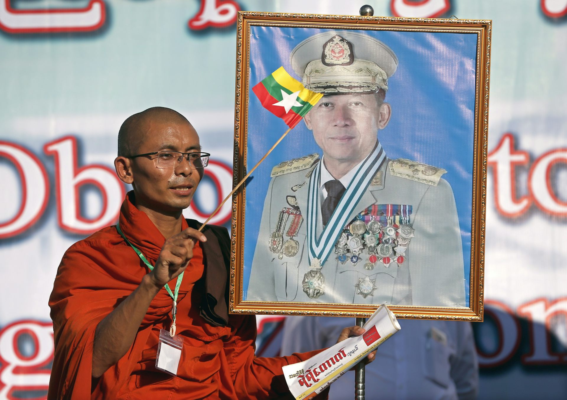 A Buddhist monk waves the Myanmar national flag as he holds a portrait of Myanmar military chief Min Aung Hlaing.