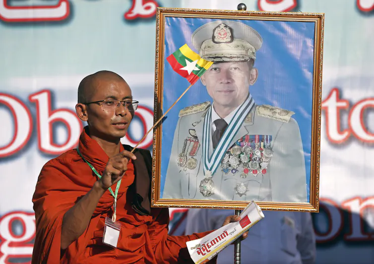 A Buddhist monk waves the Myanmar national flag as he holds a portrait of Myanmar military chief Min Aung Hlaing.